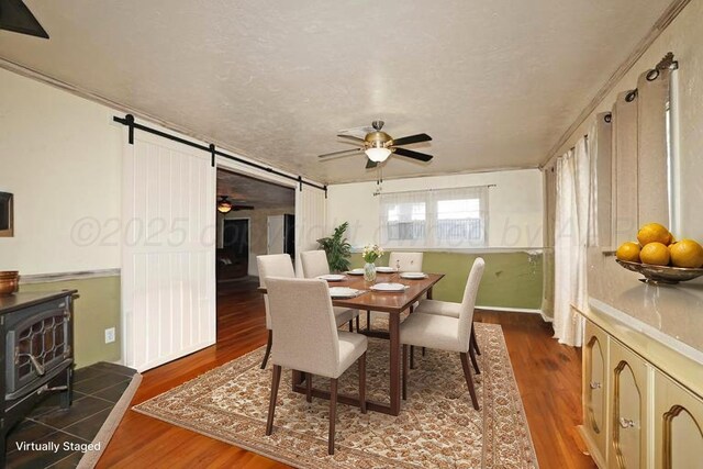 dining room featuring a wood stove, a barn door, ceiling fan, and wood finished floors