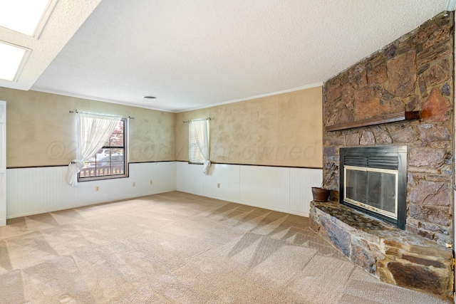 unfurnished living room featuring a textured ceiling, wainscoting, carpet flooring, a fireplace, and ornamental molding