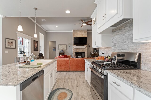 6702 Tatum Cir, Amarillo, TX 79119 - kitchen featuring stainless steel appliances, a sink, ceiling fan, a stone fireplace, and light wood-style flooring