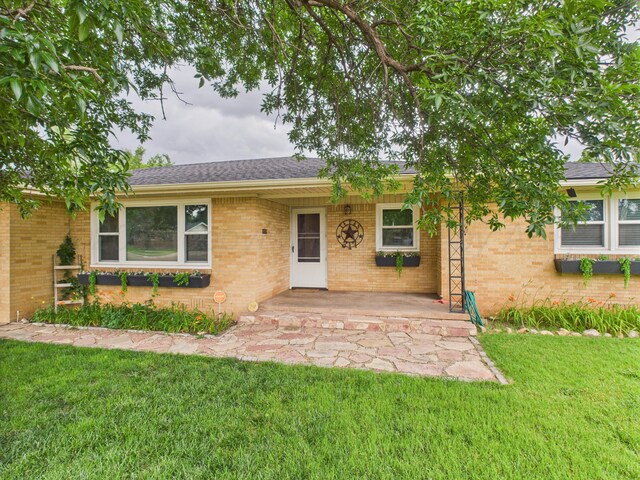 317 Morton Ave, Dumas, TX 79029 - view of front of home featuring a front lawn, brick siding, covered porch, and roof with shingles
