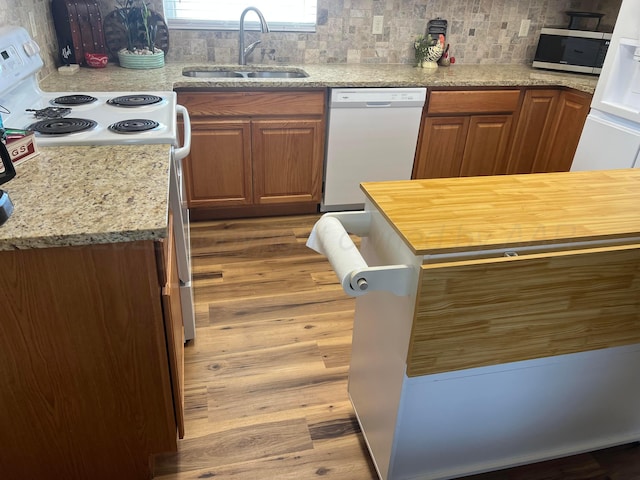 kitchen featuring backsplash, wood finished floors, brown cabinetry, white appliances, and a sink