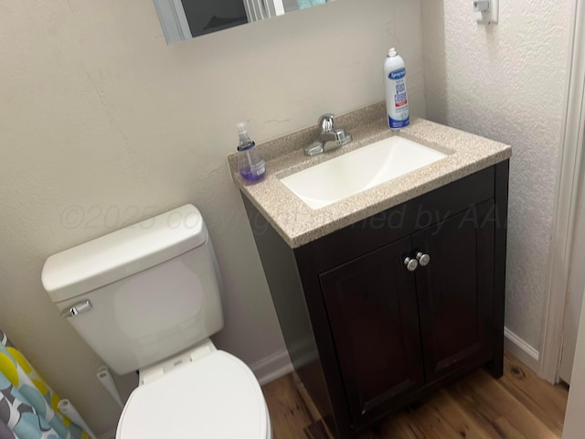 half bathroom with toilet, vanity, baseboards, and wood finished floors