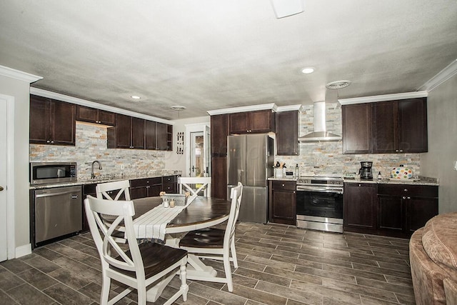 kitchen with wall chimney exhaust hood, appliances with stainless steel finishes, wood finish floors, and dark brown cabinetry