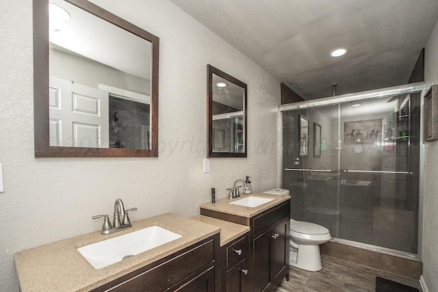 bathroom with a stall shower, a textured wall, toilet, wood finished floors, and vanity