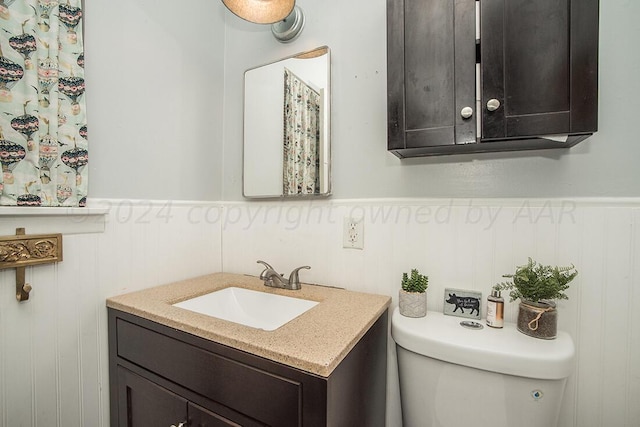 bathroom with toilet, vanity, and wainscoting