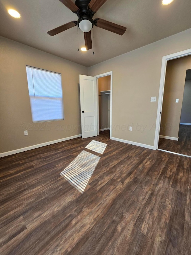 unfurnished bedroom featuring a walk in closet, dark wood-type flooring, a closet, and ceiling fan