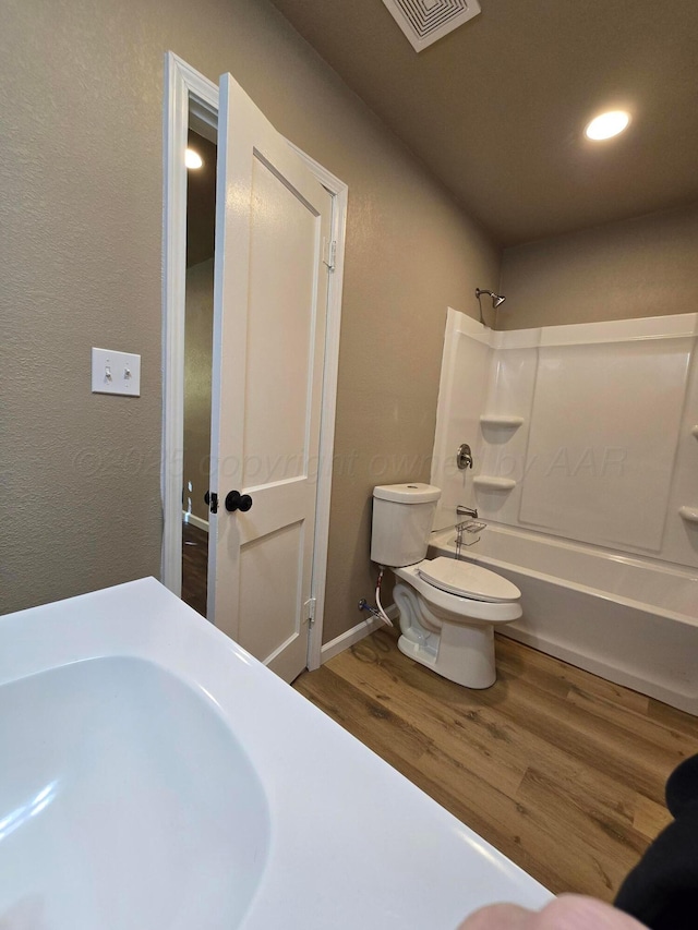 bathroom featuring hardwood / wood-style flooring, washtub / shower combination, and toilet