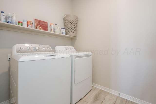 clothes washing area with washing machine and dryer, laundry area, light wood finished floors, and baseboards