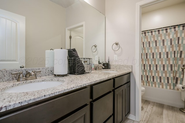 bathroom featuring double vanity, wood finished floors, a sink, and toilet