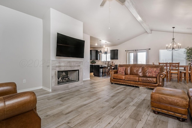 living room with beamed ceiling, light wood-type flooring, a fireplace, high vaulted ceiling, and ceiling fan with notable chandelier