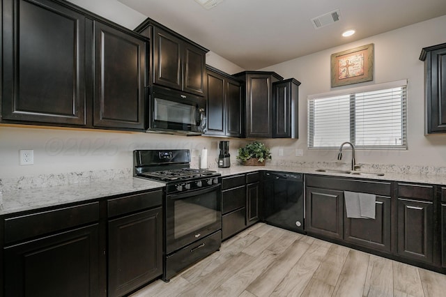 kitchen with visible vents, light wood-style flooring, a sink, light stone countertops, and black appliances