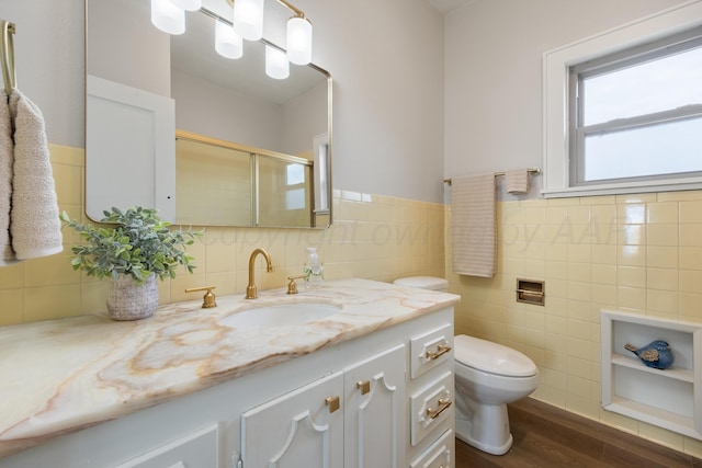 bathroom featuring wood-type flooring, tile walls, vanity, toilet, and a shower with door