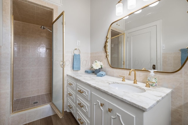 bathroom featuring vanity, wood-type flooring, tile walls, and a shower with shower door