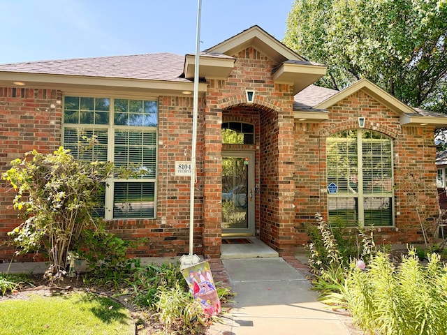 doorway to property with roof with shingles and brick siding