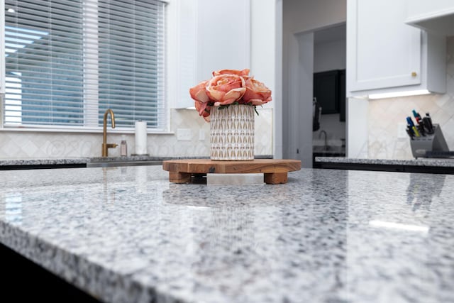 details featuring tasteful backsplash, light stone counters, white cabinetry, and a sink