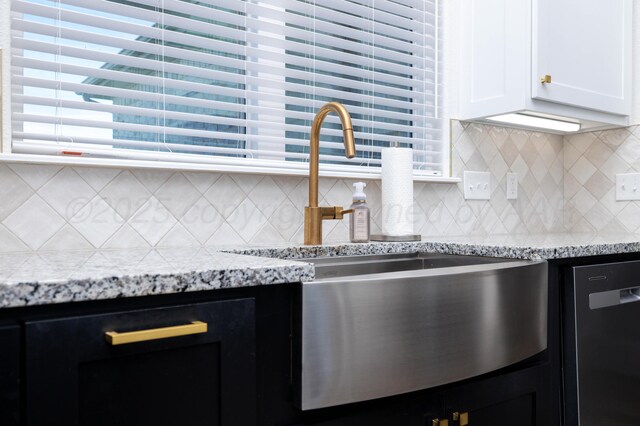 kitchen with light stone counters, a sink, dark cabinetry, white cabinetry, and dishwashing machine
