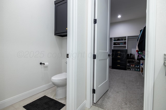 bathroom featuring a walk in closet, toilet, and baseboards