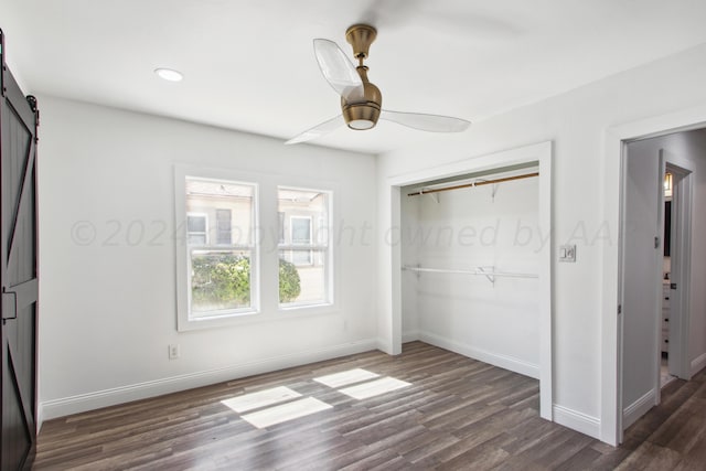 unfurnished bedroom with dark wood-type flooring, a closet, a barn door, and ceiling fan