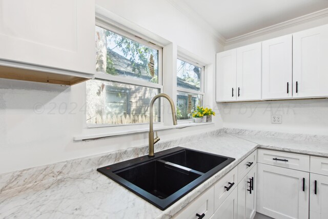 kitchen with white cabinets, light stone countertops, sink, and crown molding