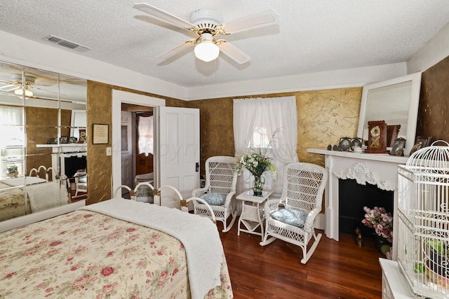bedroom featuring wood finished floors, a textured ceiling, a ceiling fan, and a high end fireplace