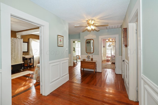 corridor featuring a wainscoted wall, hardwood / wood-style flooring, a chandelier, and a textured ceiling