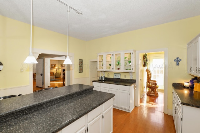 kitchen featuring dark countertops, light wood-style floors, white cabinetry, glass insert cabinets, and a textured ceiling