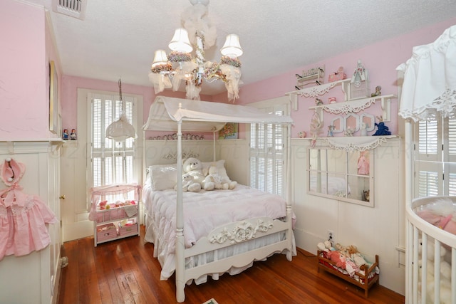 bedroom with wood-type flooring, a chandelier, a textured ceiling, and wainscoting