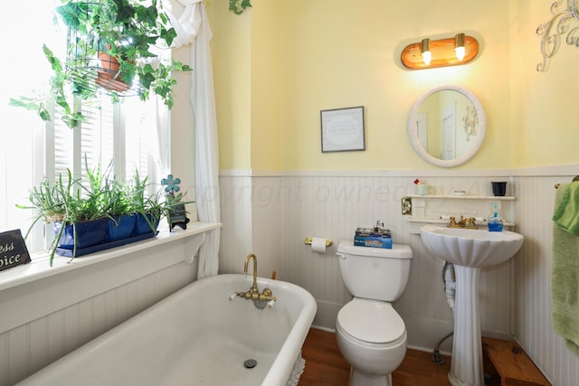 full bathroom featuring a wainscoted wall, a soaking tub, toilet, wood finished floors, and a sink