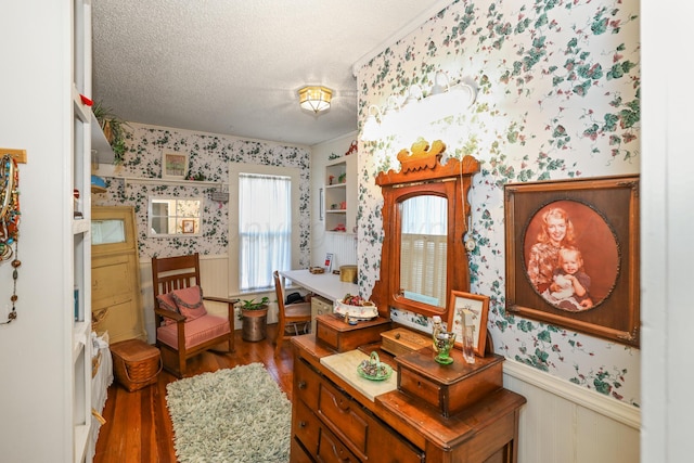 living area featuring wallpapered walls, wainscoting, wood finished floors, and a textured ceiling