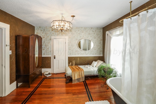 bedroom featuring hardwood / wood-style floors, wallpapered walls, a chandelier, and a textured ceiling