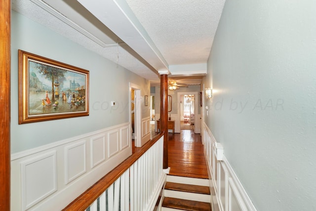 corridor with a textured ceiling, wood finished floors, a decorative wall, and wainscoting