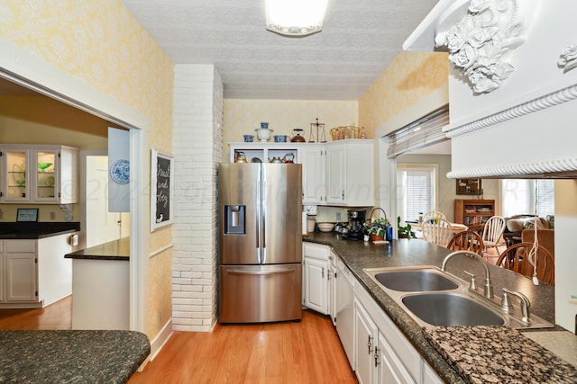 kitchen with stainless steel fridge with ice dispenser, wallpapered walls, a sink, white cabinets, and dark countertops