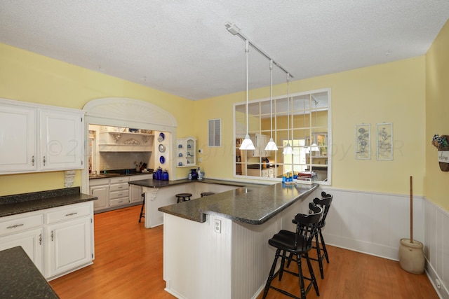 kitchen with a breakfast bar area, light wood-style flooring, white cabinets, a textured ceiling, and wainscoting