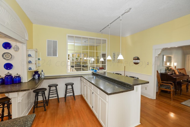 kitchen with wood finished floors, dark countertops, a peninsula, a textured ceiling, and white cabinets