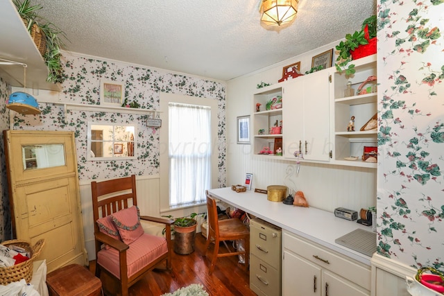 office area featuring wallpapered walls, dark wood-style flooring, a textured ceiling, a wainscoted wall, and crown molding
