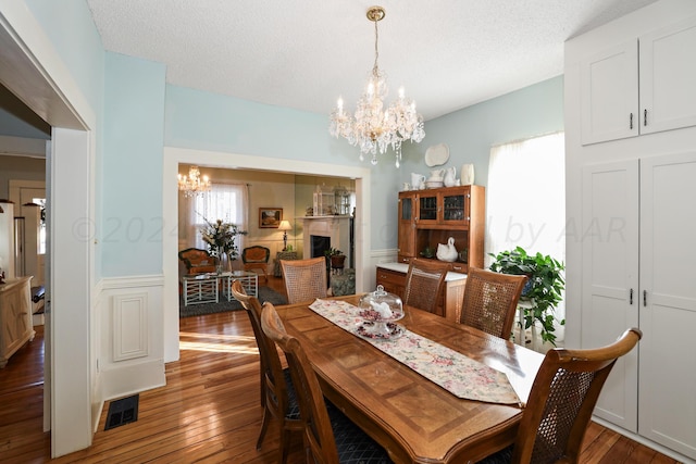 dining area with a chandelier, hardwood / wood-style floors, a textured ceiling, and wainscoting