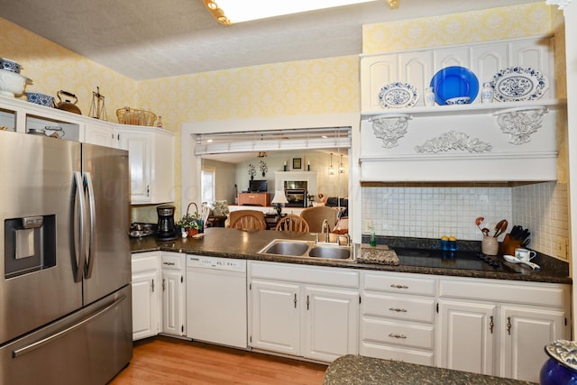 kitchen featuring stainless steel fridge, dishwasher, wallpapered walls, a sink, and white cabinetry