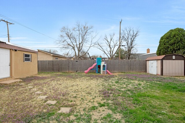 fenced backyard featuring a storage unit, an outdoor structure, and a playground