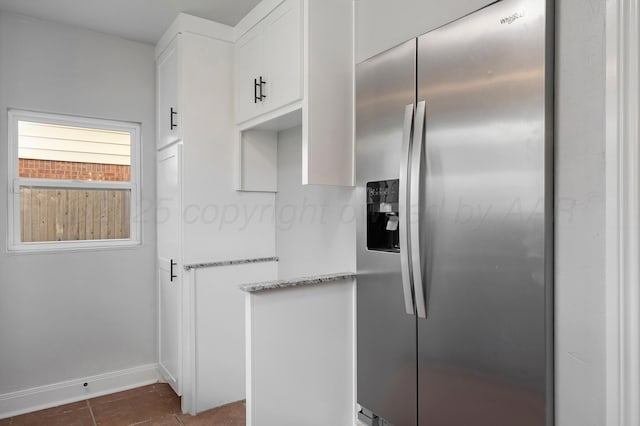 kitchen featuring stainless steel refrigerator with ice dispenser, light stone countertops, baseboards, white cabinets, and dark tile patterned floors