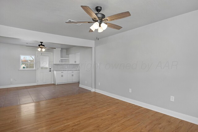 unfurnished living room with ceiling fan, light wood finished floors, and baseboards