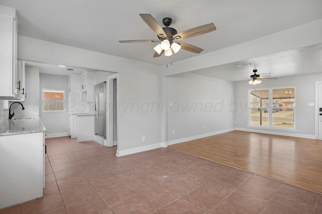 unfurnished living room with ceiling fan, a sink, baseboards, and tile patterned floors