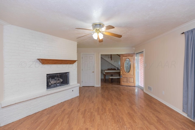 unfurnished living room featuring baseboards, visible vents, a ceiling fan, wood finished floors, and a brick fireplace
