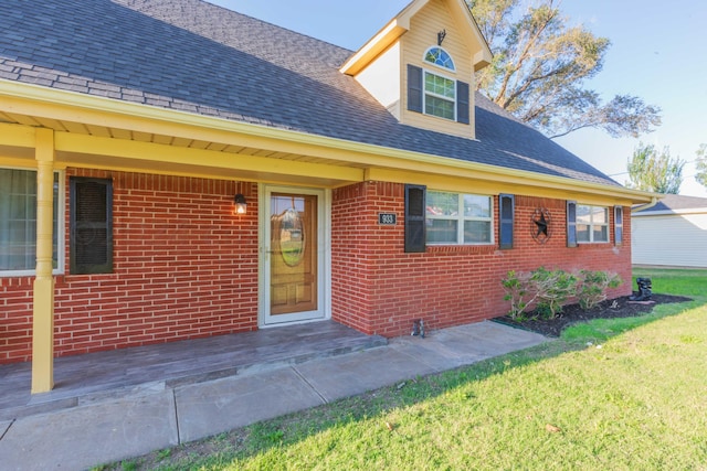 view of front of home with a front lawn, brick siding, and roof with shingles