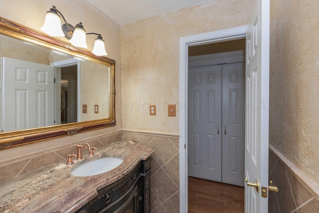 bathroom featuring vanity, wood finished floors, a wainscoted wall, and tile walls