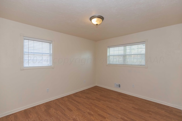 empty room featuring baseboards, wood finished floors, and visible vents