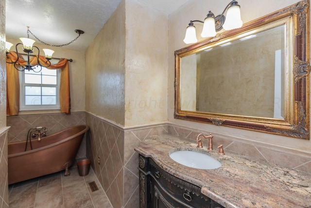 full bathroom with a wainscoted wall, tile walls, a notable chandelier, a freestanding tub, and vanity