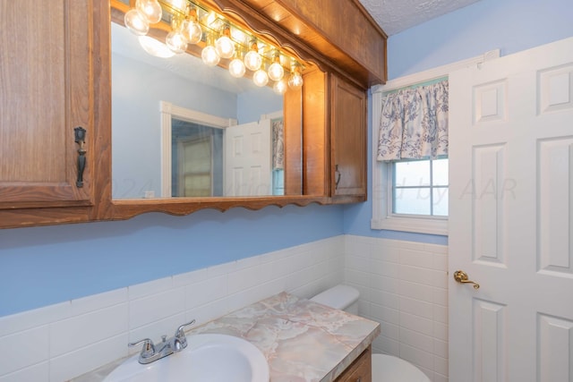 bathroom with tile walls, wainscoting, vanity, and toilet
