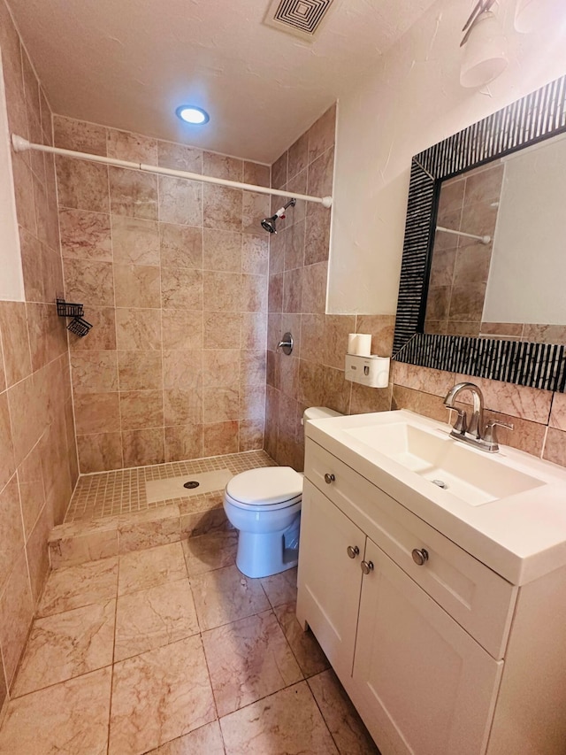 bathroom featuring vanity, toilet, tile walls, visible vents, and tiled shower