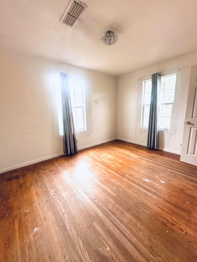 spare room featuring a healthy amount of sunlight, baseboards, hardwood / wood-style floors, and visible vents