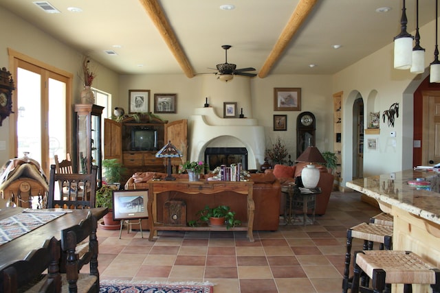 tiled living room featuring ceiling fan, a fireplace, and beamed ceiling